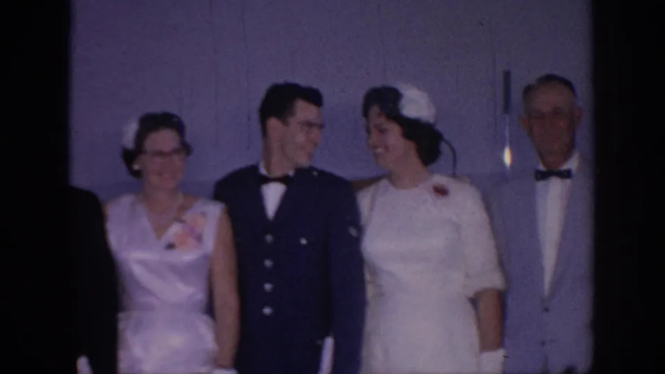 The groom and bride turn toward one another during the 1967 Oklahoma wedding pose, with guests partly visible at the edges of the frame.