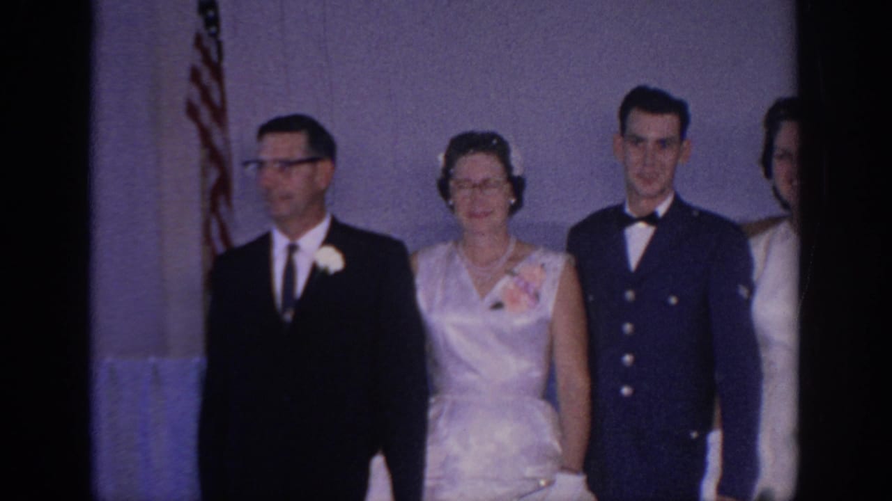 Formal wedding group faces the camera with an American flag behind them and the bride partly cropped at right.
