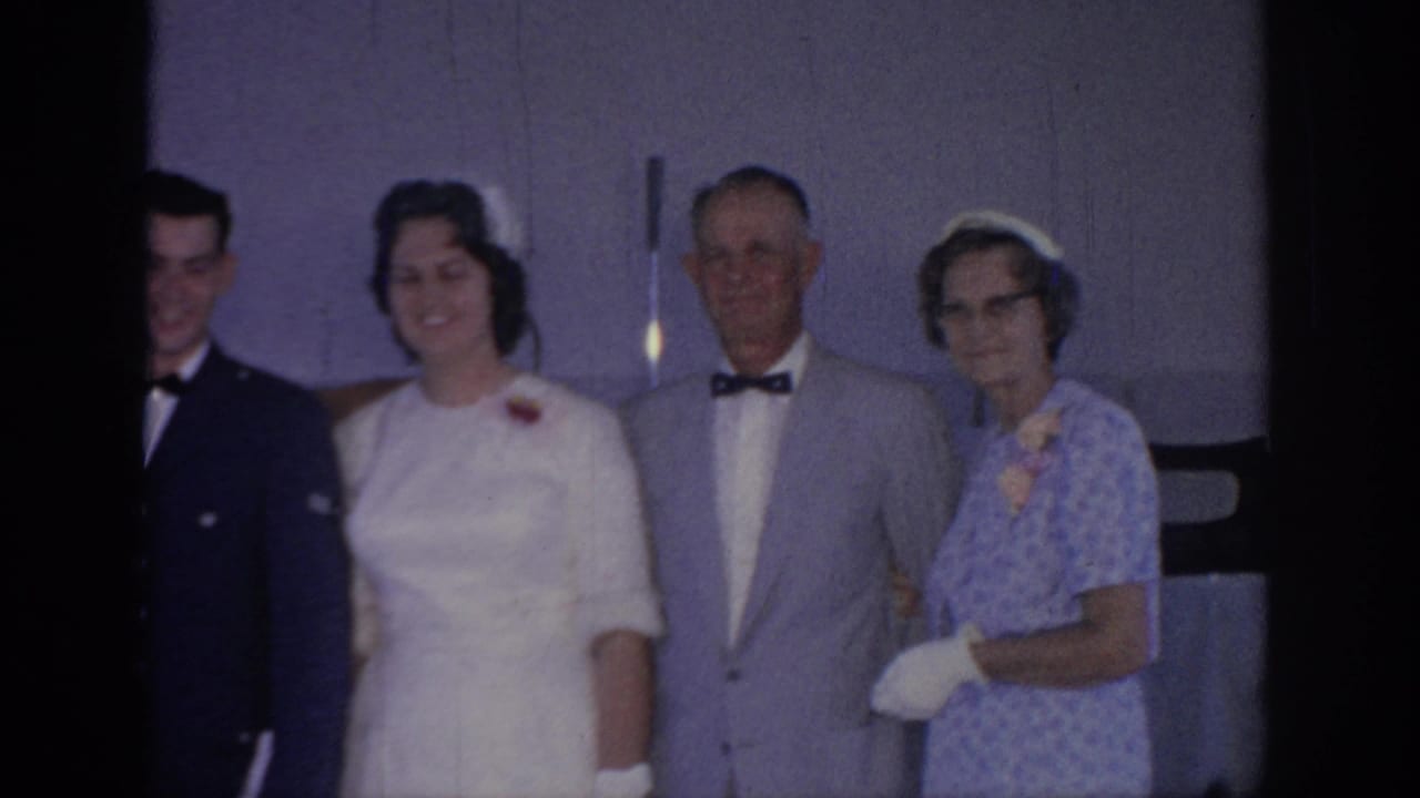 1967 Oklahoma home-movie frame of a wedding group posing indoors, with a bride in white beside an older man and woman.