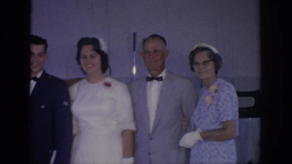 1967 Oklahoma home-movie frame of a wedding group posing indoors, with a bride in white beside an older man and woman.