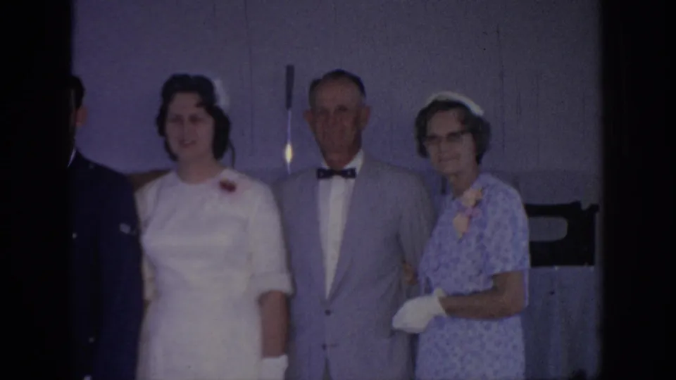 A soft 1967 Oklahoma 8mm frame shows the bride, an older man, and an older woman posing during a wedding gathering.