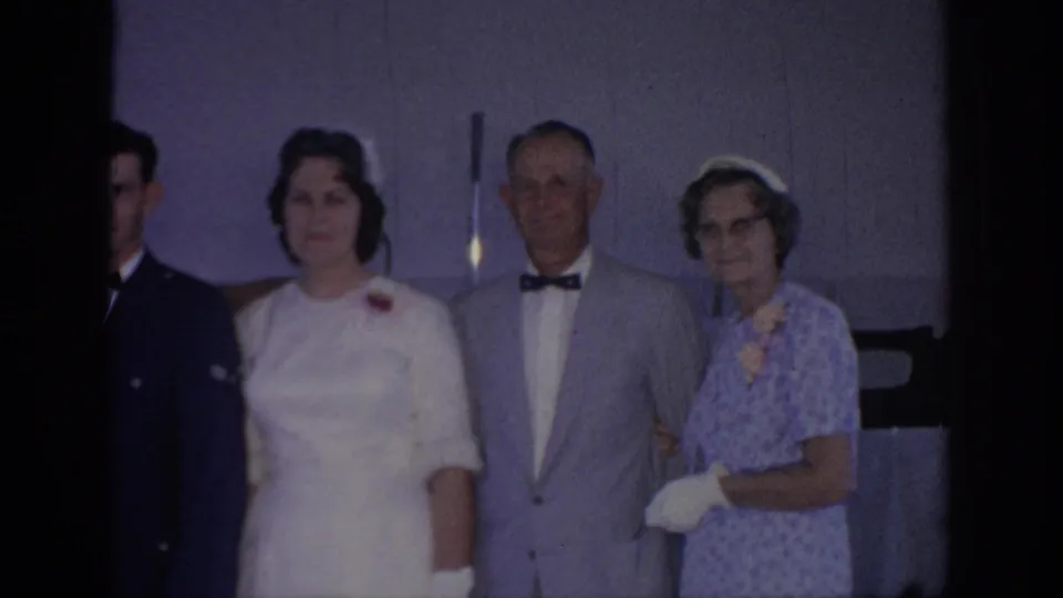 1967 Oklahoma home-movie frame with a bride and older couple posing indoors while a uniformed figure is partly visible at left.