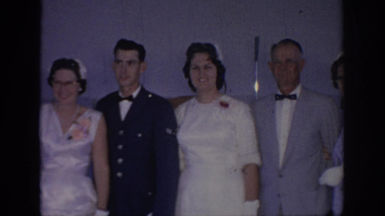 Bride stands beside a man in dark military uniform and older family members.