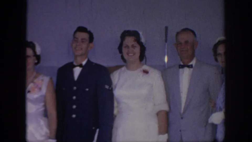 1967 Oklahoma frame showing a uniformed man beside a woman in a white dress and an older suited man at a formal indoor event.