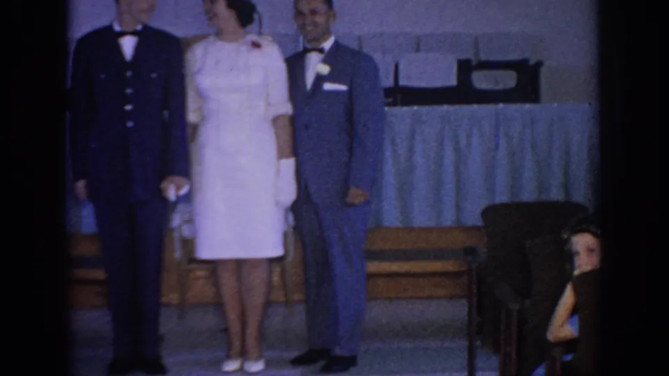 1967 Oklahoma frame with formally dressed adults near banquet seating, cropped by the contact-sheet border and dim indoor exposure.