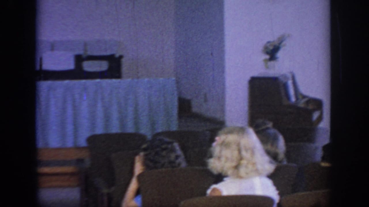 Guests sit in rows facing the front of a hall with chairs and a curtained table visible.