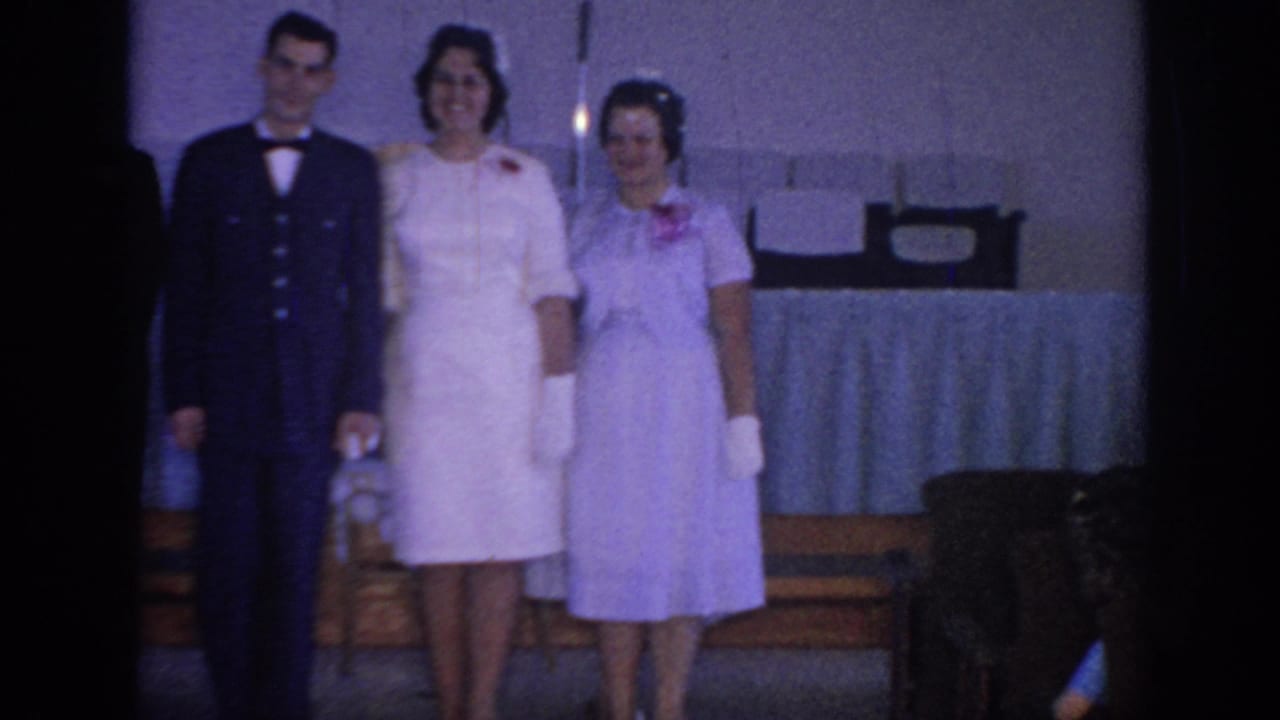 Three adults posing in formal clothing, including a man in a dark uniform and two women in light dresses.