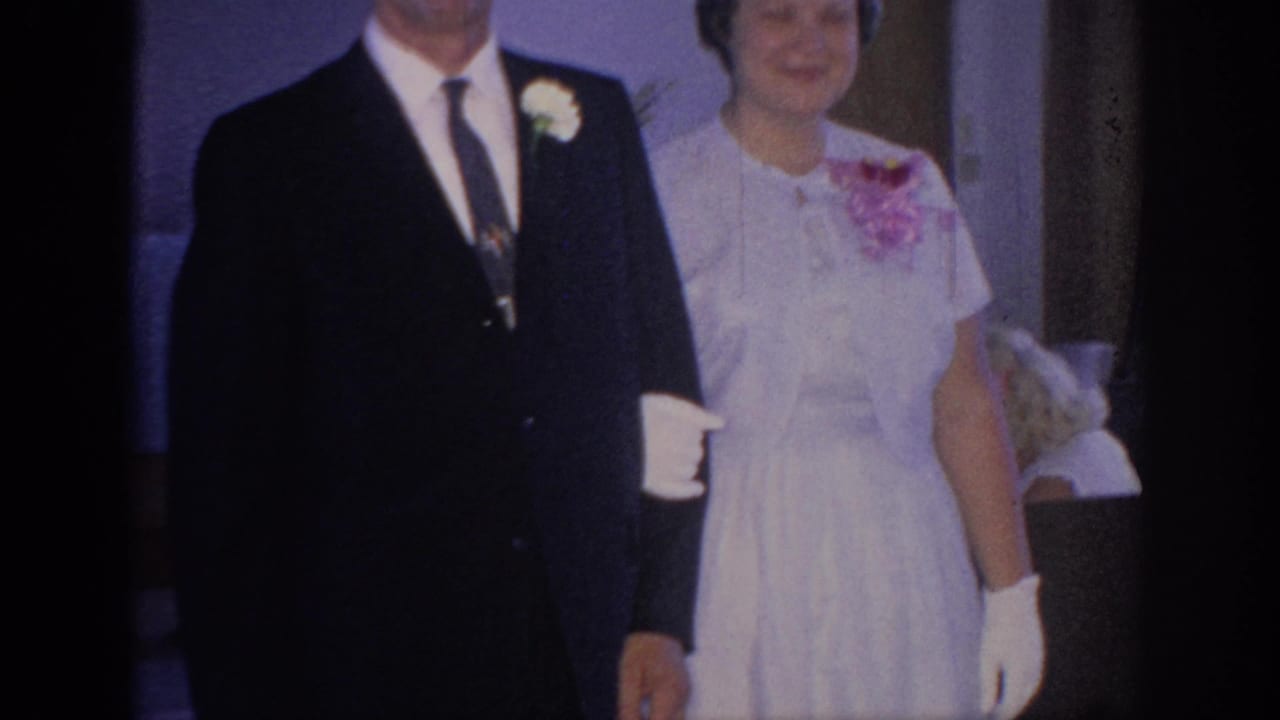 Formal couple stands or walks together, with a woman in white wearing a corsage.