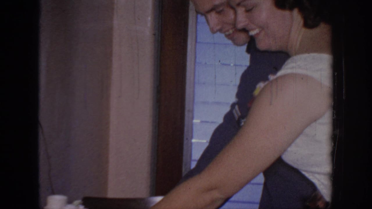 In supported 1967 Oklahoma home-movie footage, a smiling couple stands close near a table during a wedding or anniversary cake moment.