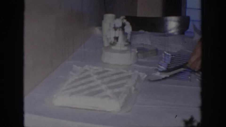 The white frosted cake rests on the table after cutting, with the small ornament still visible in the indoor Oklahoma celebration footage.