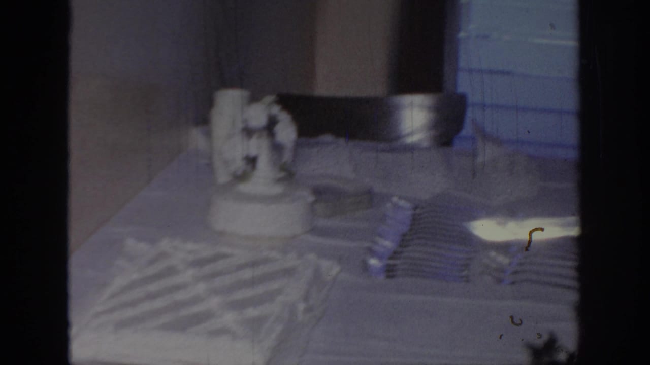 1967 Oklahoma 8mm frame showing a white frosted wedding cake, stacked forks, and table setting in an indoor reception space.