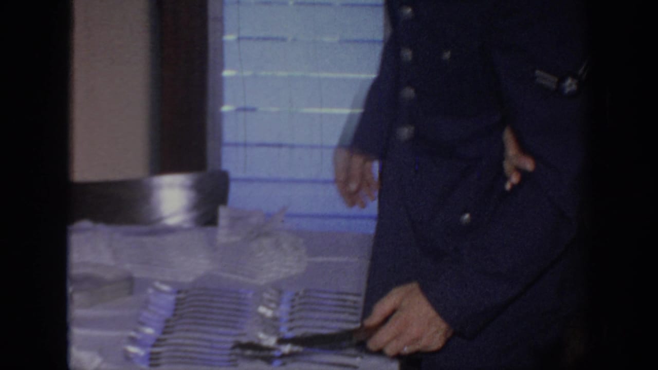 Uniformed man reaches toward a cake knife beside the wedding table.