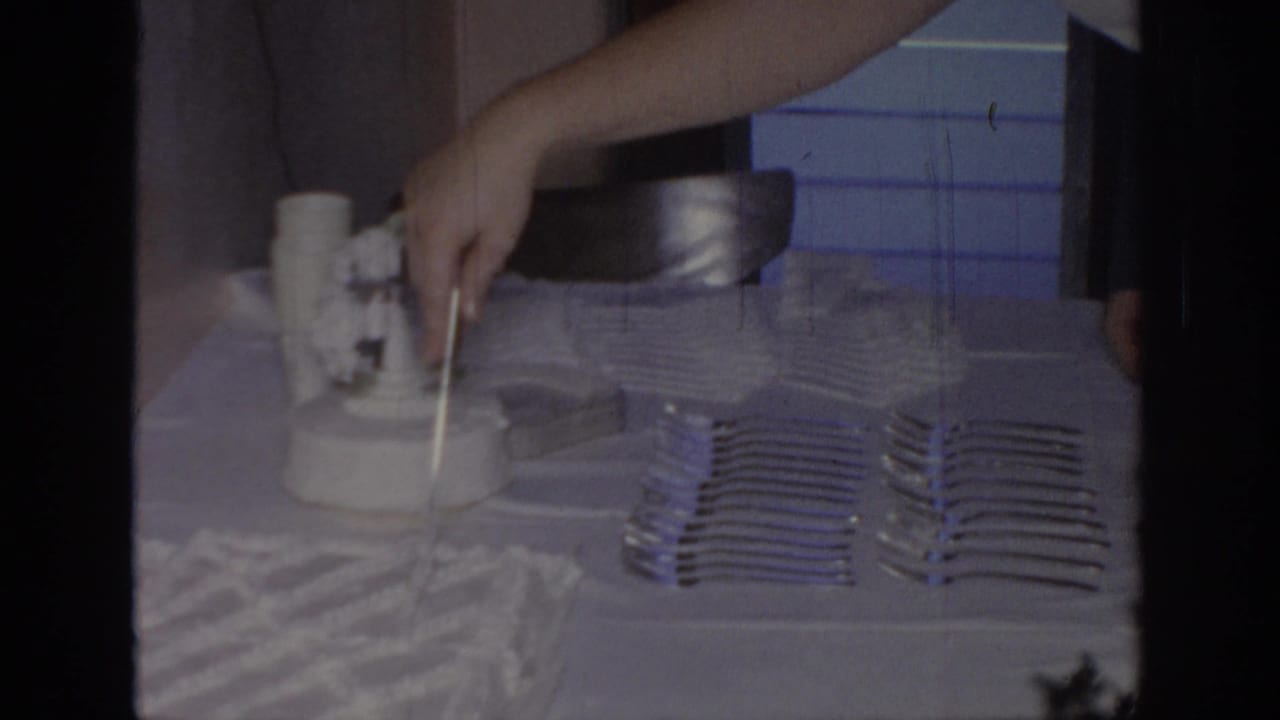 Hand holds a knife over a white cake with rows of forks arranged beside it.
