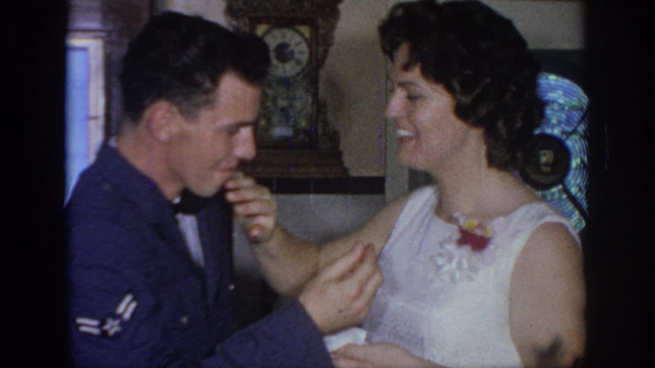In 1967 Oklahoma home-movie footage, a uniformed man and bride smile while sharing cake in a private interior.