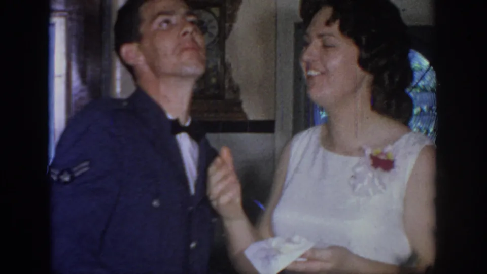 The uniformed man looks up playfully as the bride laughs, holding cake in a 1967 Oklahoma wedding scene.