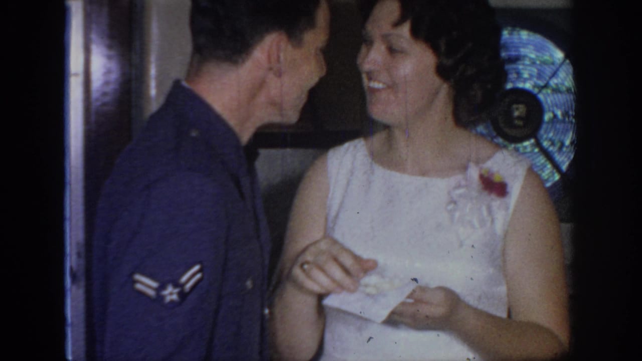 In 1967 Oklahoma home-movie footage, an Air Force serviceman faces a smiling woman in a white sleeveless dress with a corsage.