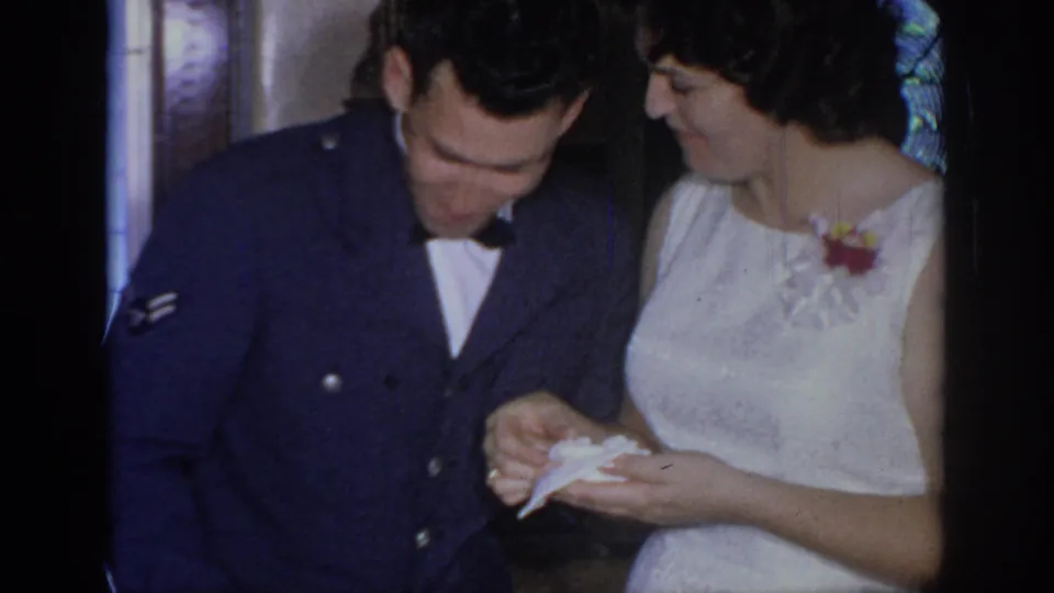 The Air Force serviceman and woman in a white dress appear to examine a small paper or card during the Oklahoma wedding scene.