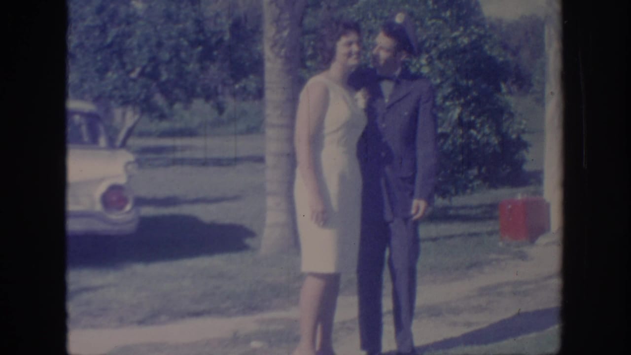 Couple stands close together near a classic car and trees.