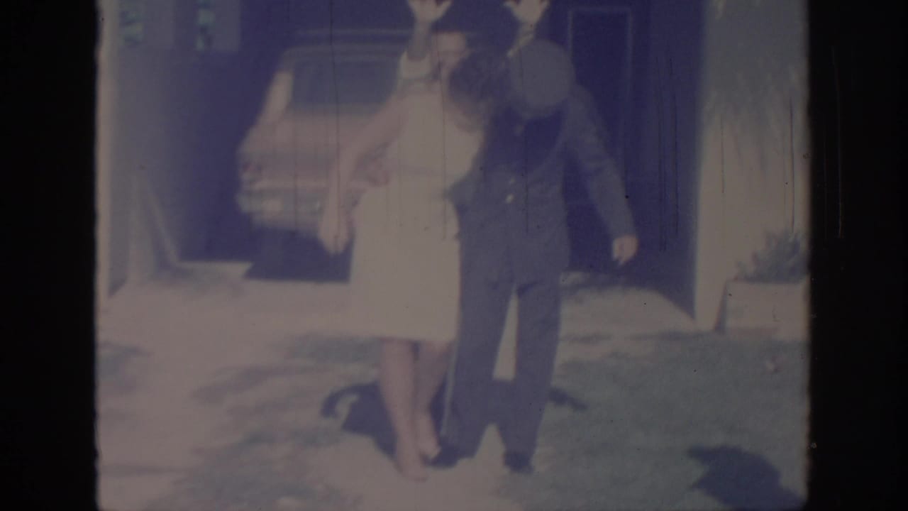 Woman and uniformed man continue posing outside, with a parked car behind them.