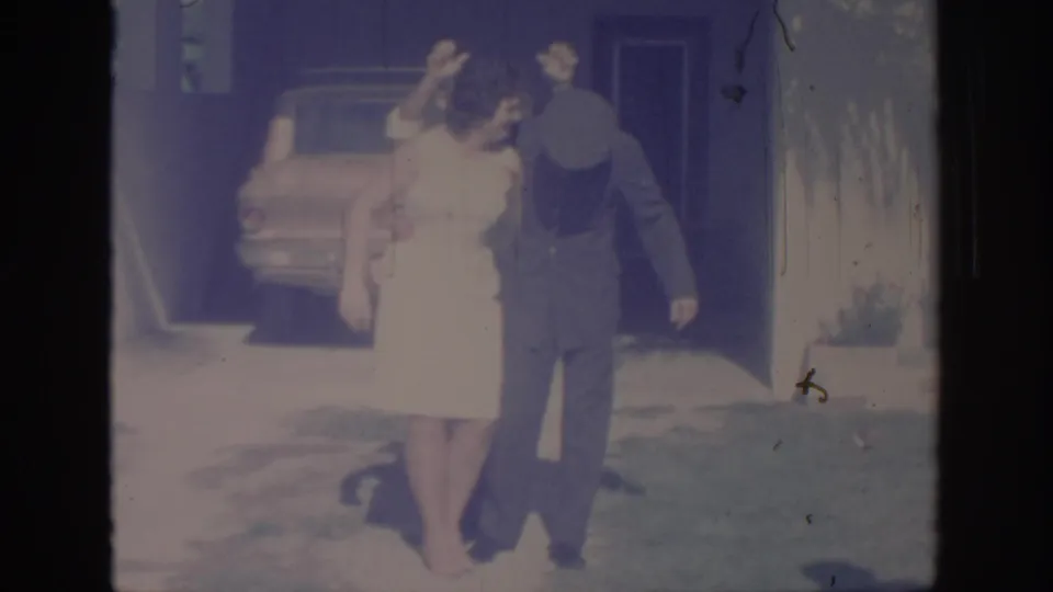 Faded 8mm frame from Oklahoma in 1967 showing a woman gesturing beside a uniformed man outside a home.