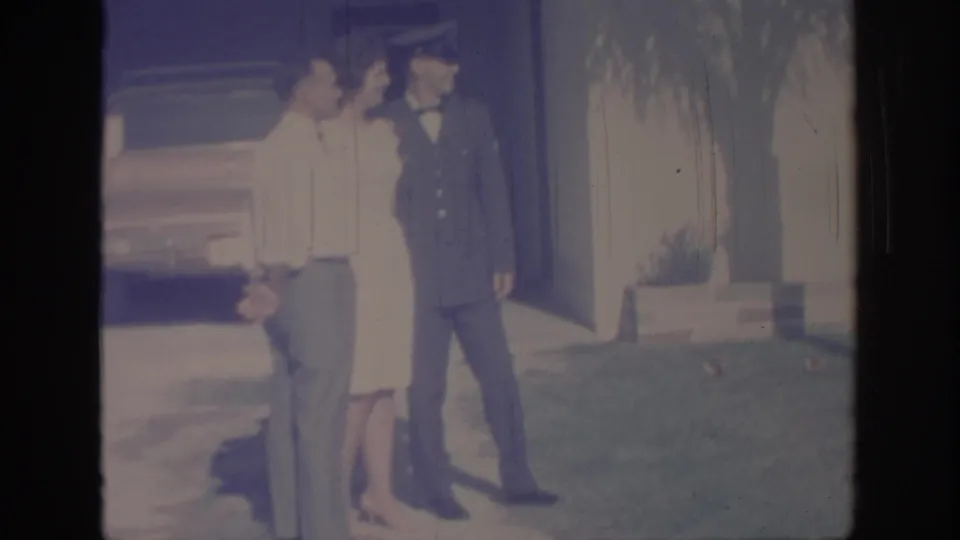 1967 Oklahoma home-movie frame showing three adults gathered outside, with one wearing a formal military uniform.