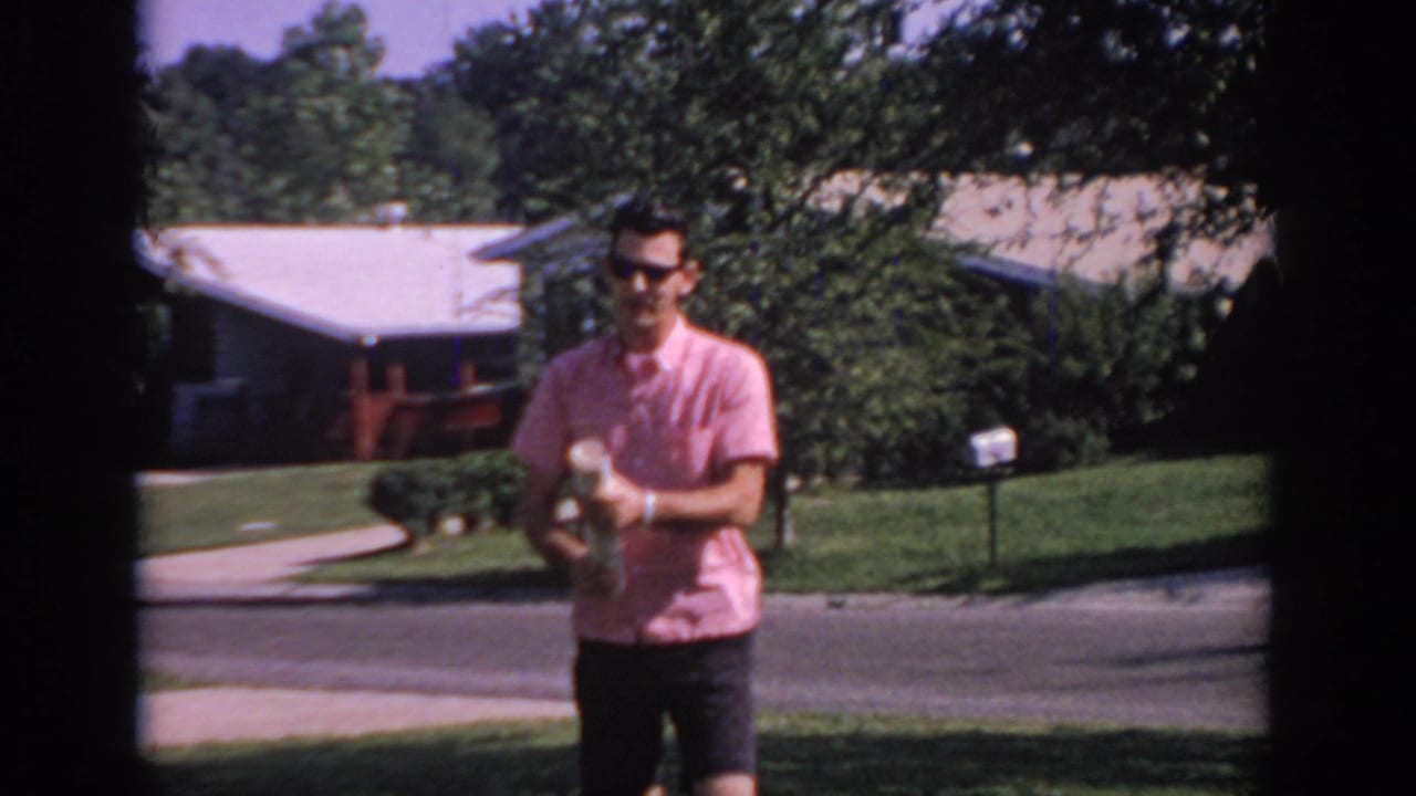 In 1967 Oklahoma home-movie footage, a young man in a pink short-sleeve shirt holds a rolled newspaper on a sunny suburban lawn.
