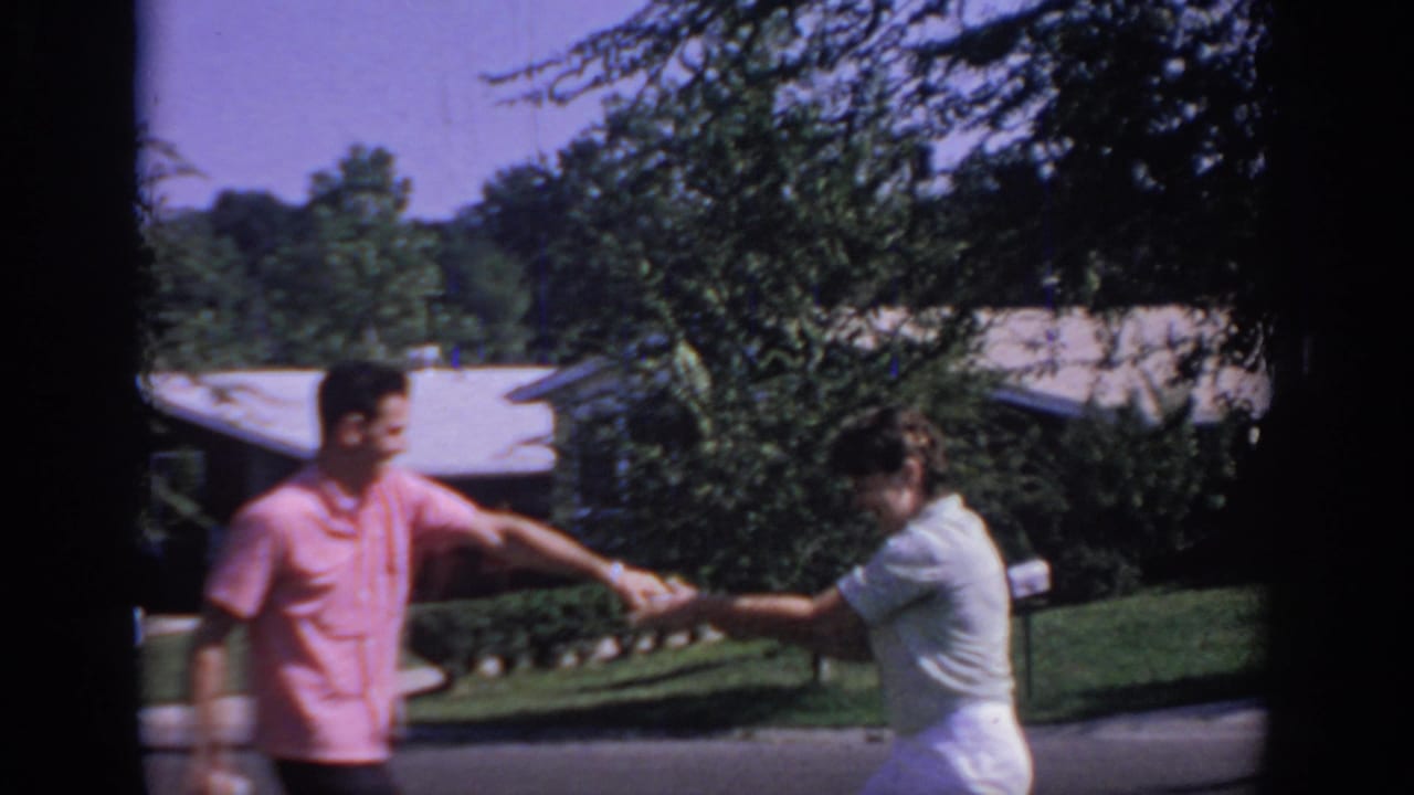 In 1967 Oklahoma home-movie footage, a man in a pink shirt and a woman in white begin a playful newspaper tug-of-war near lawns and houses.