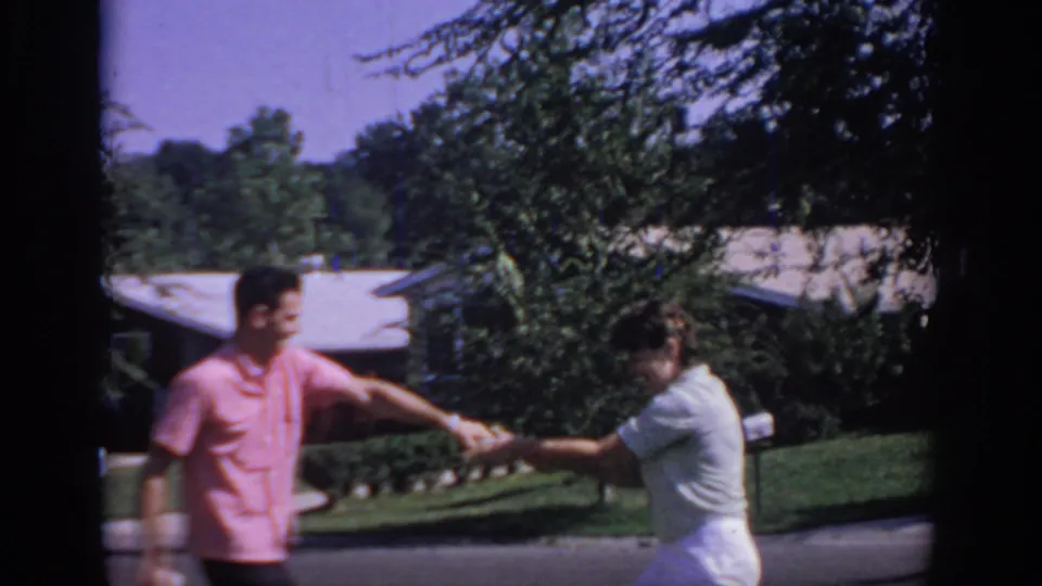 In 1967 Oklahoma home-movie footage, a man in a pink shirt and a woman in white begin a playful newspaper tug-of-war near lawns and houses.