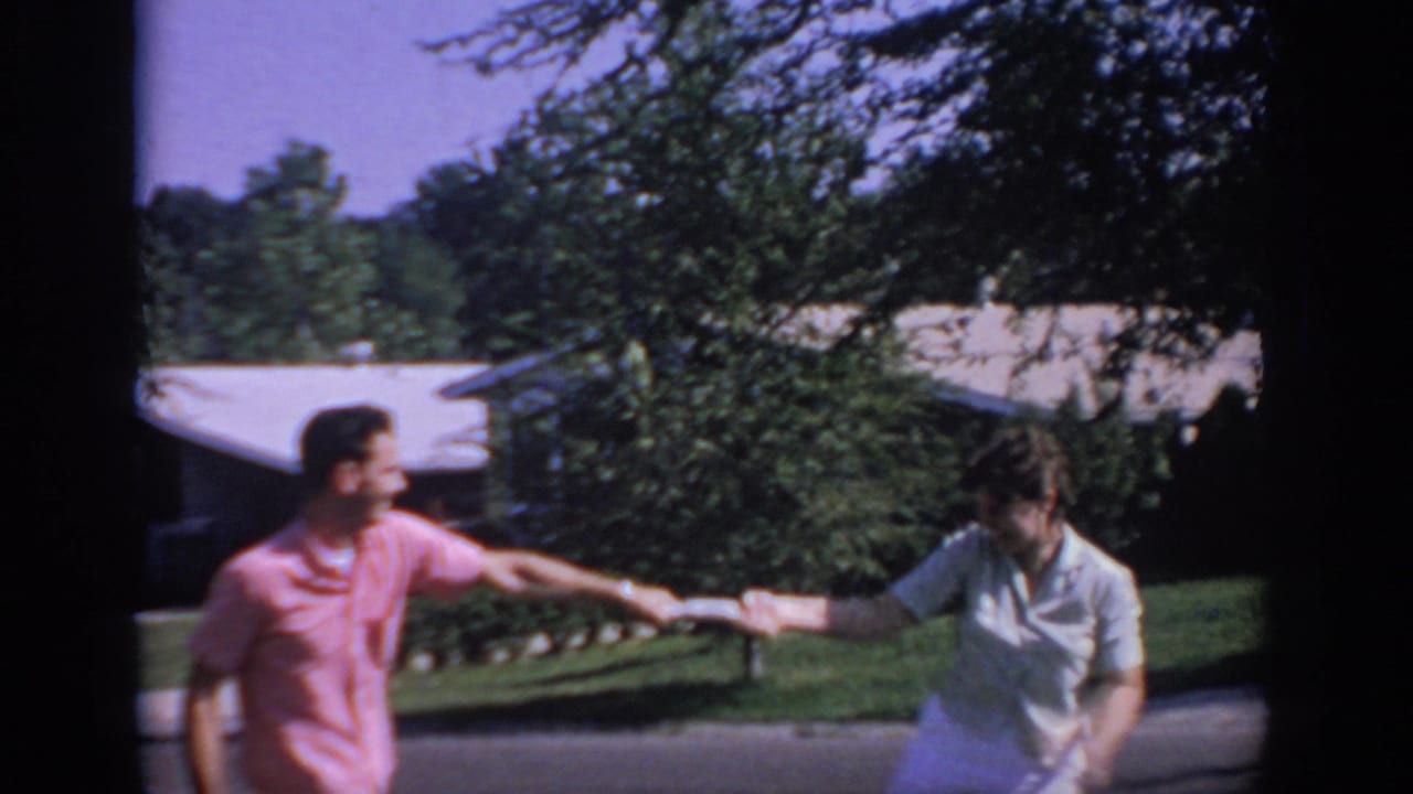 The two adults continue the tug-of-war in the Oklahoma suburban setting, with trees, lawn, and a low house behind them.