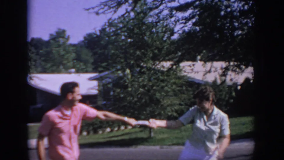 The two adults continue the tug-of-war in the Oklahoma suburban setting, with trees, lawn, and a low house behind them.