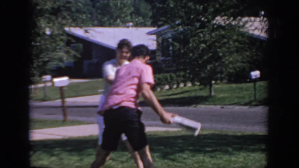 At the end of the playful exchange, the man turns with the newspaper while the woman remains nearby in the suburban Oklahoma street scene.
