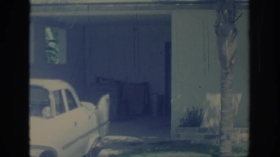 1967 Oklahoma 8mm frame showing a white classic American car beside a palm tree and covered garage.