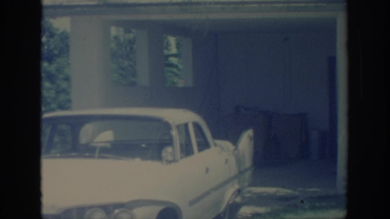 1967 Oklahoma 8mm frame showing a white mid-century car parked by a covered carport and shaded residential exterior.