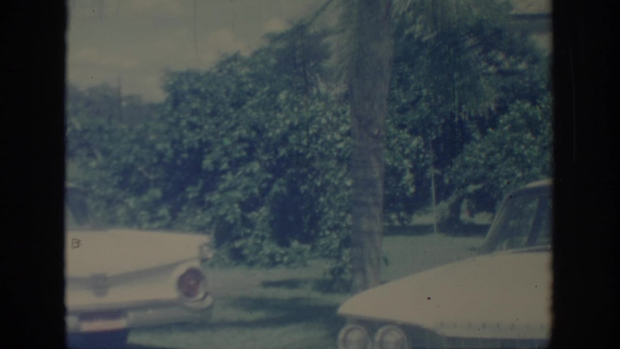 1967 Oklahoma 8mm frame showing light-colored vintage cars with tailfins near leafy trees in soft faded color.