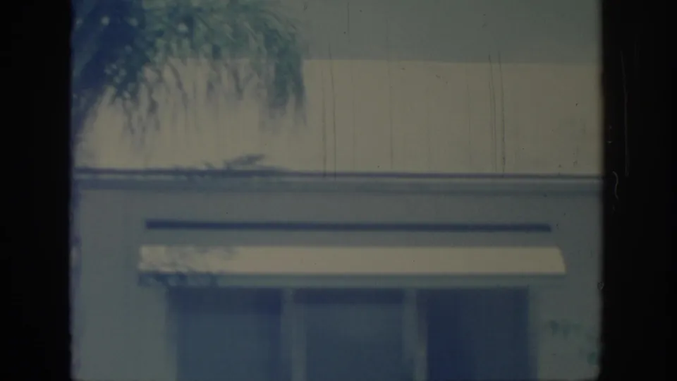 1967 Oklahoma 8mm frame showing a building edge, palm fronds, and a partial vintage car at the right edge.