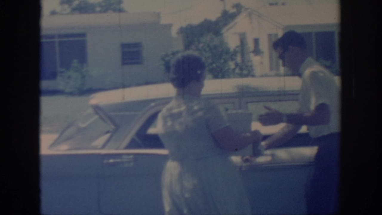 Woman in a light dress reaches a finned 1950s car where a man in a short-sleeve shirt stands nearby in Oklahoma, 1967.