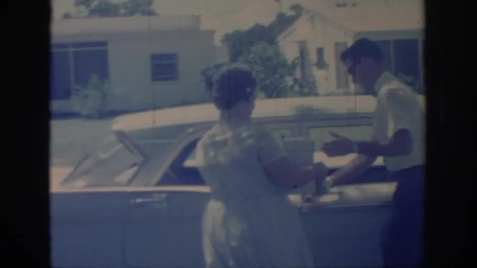 Woman in a light dress reaches a finned 1950s car where a man in a short-sleeve shirt stands nearby in Oklahoma, 1967.