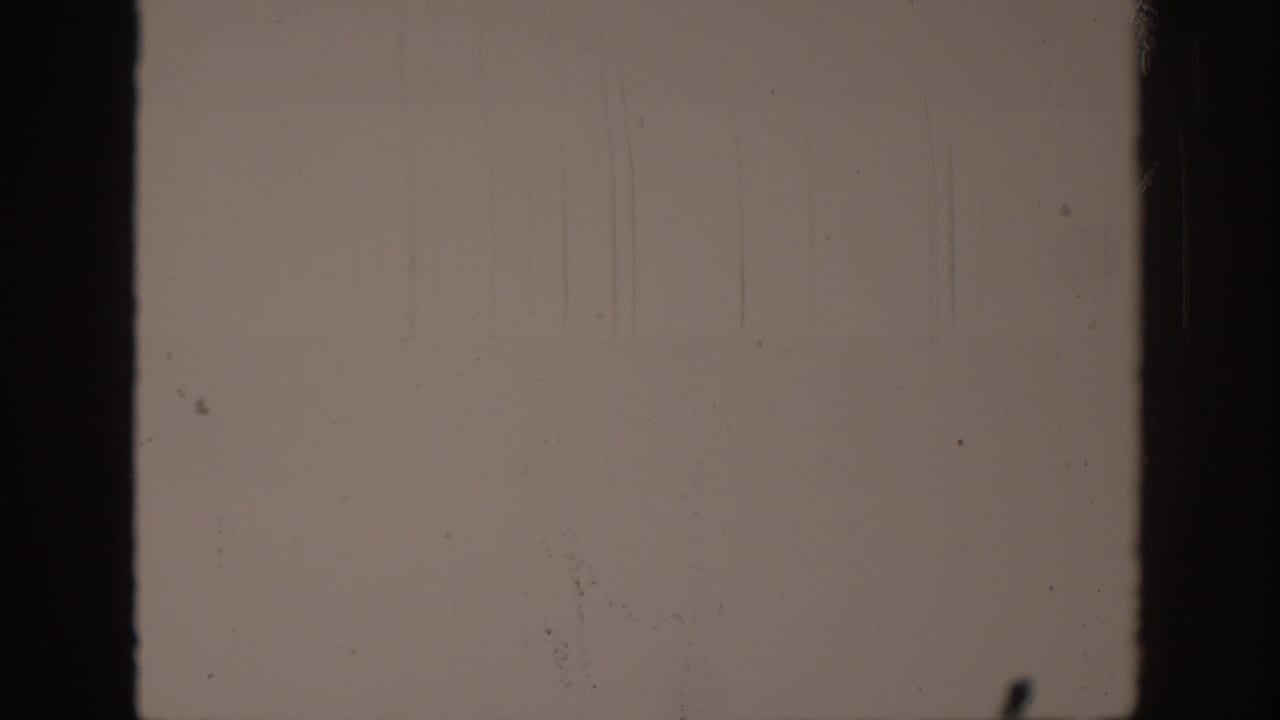 The 8mm scan shows a leader-like blank frame with vertical scratches, dust, and dark film borders.