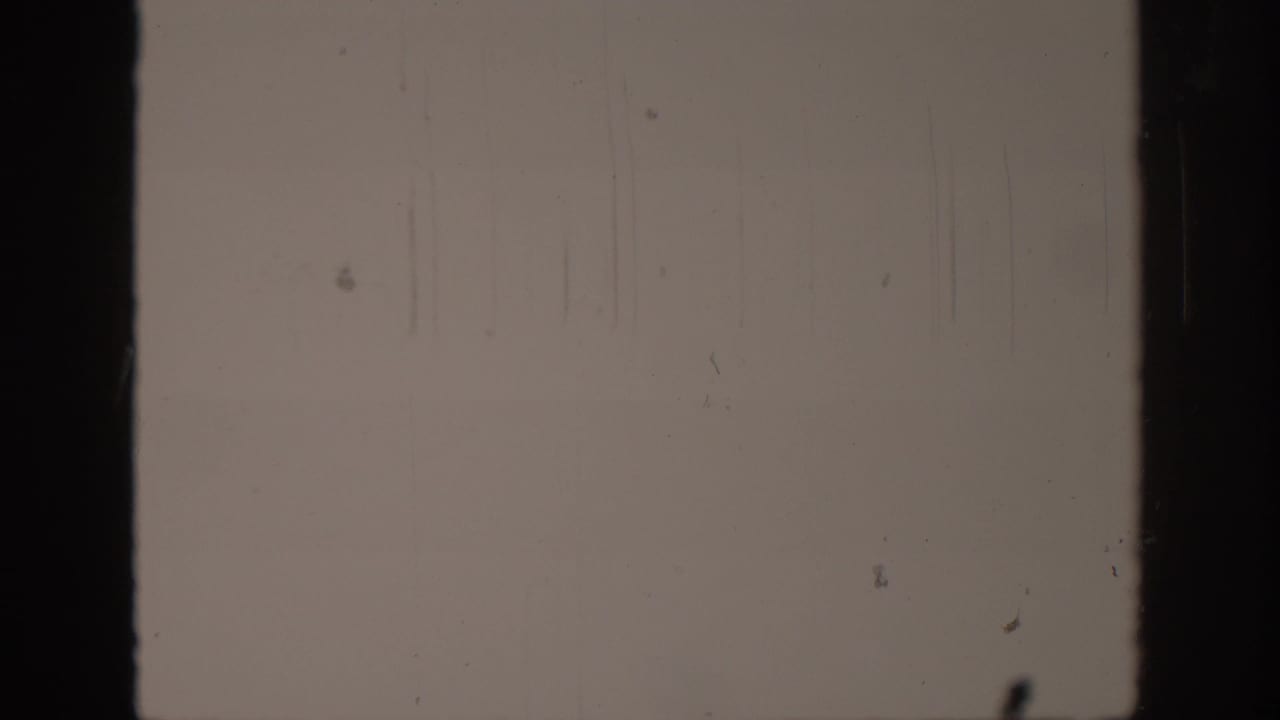 A final mostly blank 8mm frame shows vertical scratch lines, dust, and dark film edges.