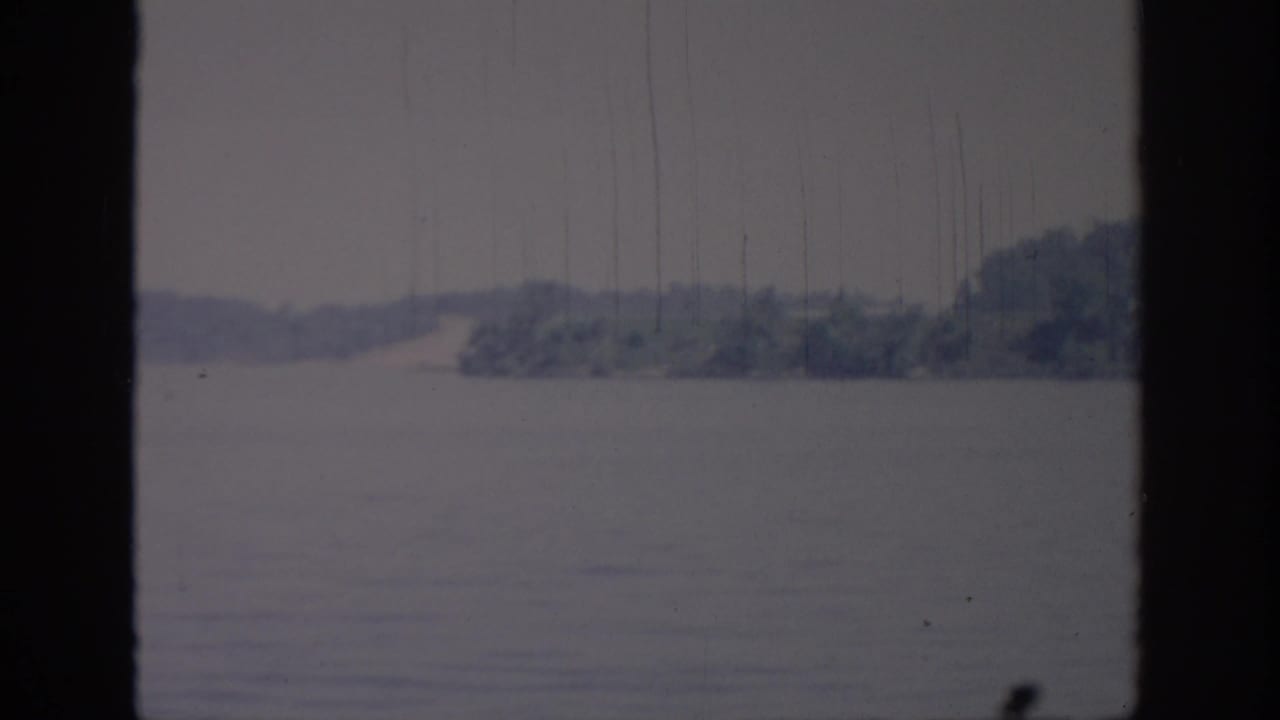 1967 Oklahoma 8mm frame showing open water, a distant wooded shore, pale sky, and dark foreground framing.