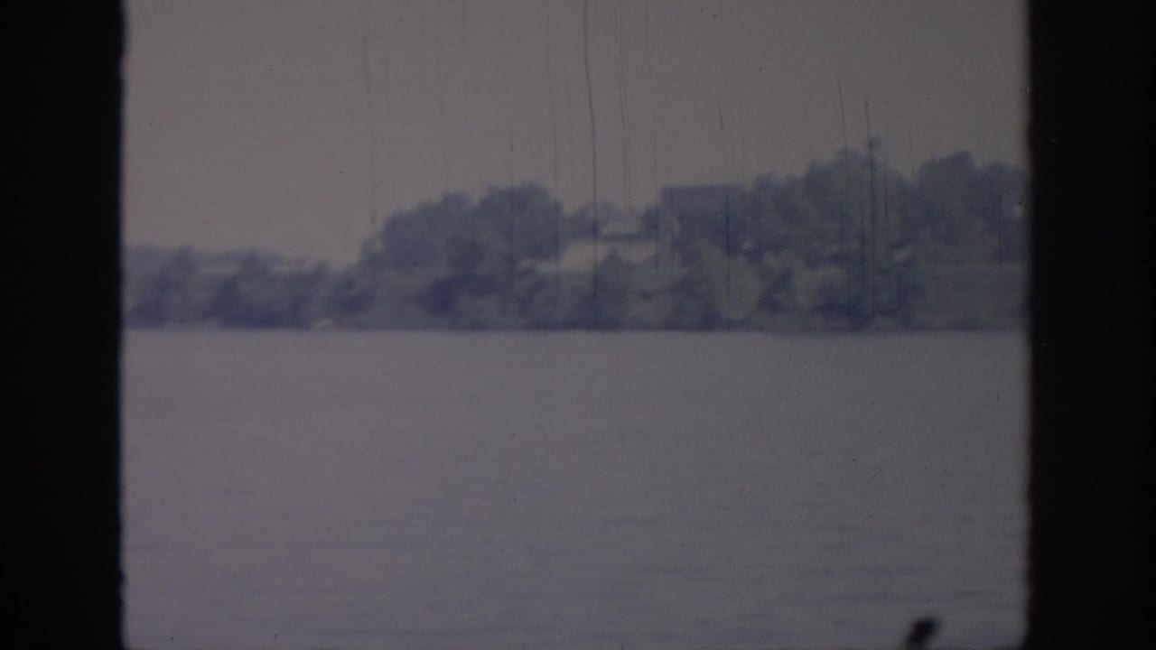1967 Oklahoma 8mm frame of a distant wooded bank across water, with soft focus and vertical film marks.