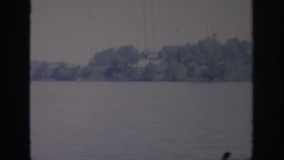 1967 Oklahoma 8mm frame of a distant wooded bank across water, with soft focus and vertical film marks.