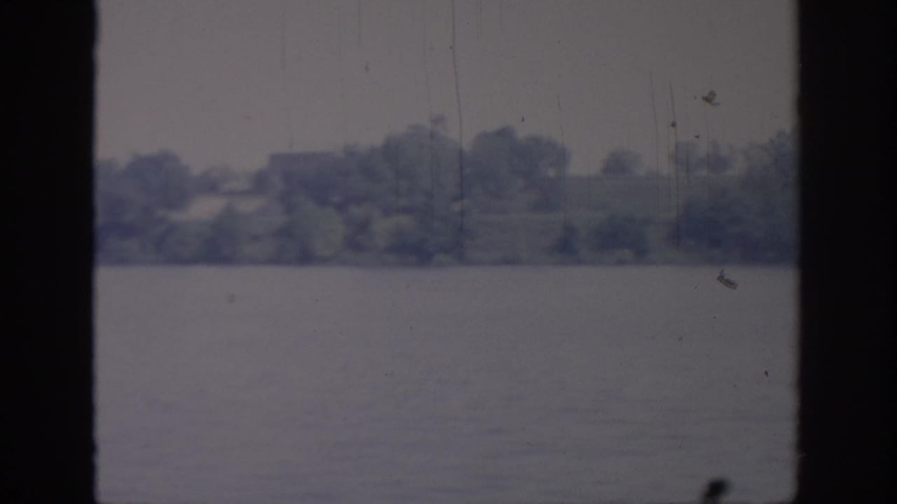 1967 Oklahoma lakeshore footage with calm water, distant trees, and visible 8mm scratches between window mullions.