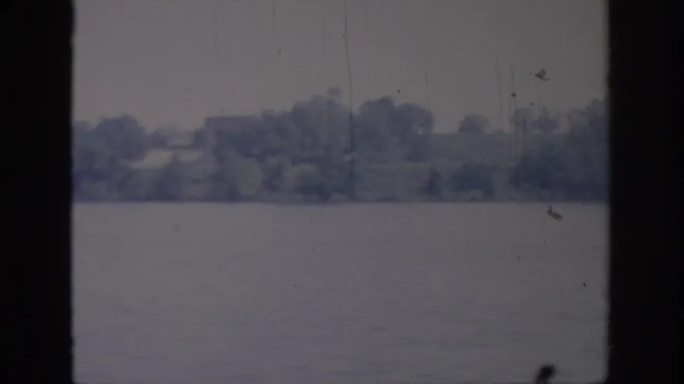 1967 Oklahoma lakeshore footage with calm water, distant trees, and visible 8mm scratches between window mullions.
