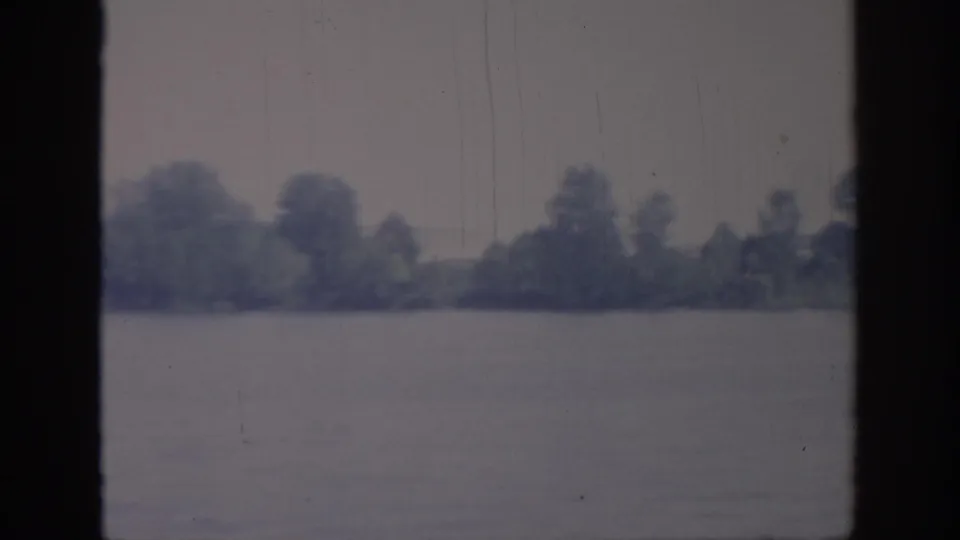 1967 Oklahoma river view from a boat, showing a low wooded shoreline across calm water with soft blue-gray color and visible film wear.
