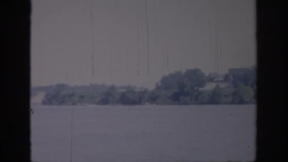 1967 Oklahoma 8mm frame showing a river channel bordered by distant trees, with soft contrast, blue-gray cast, and vertical scratch marks from the film scan.