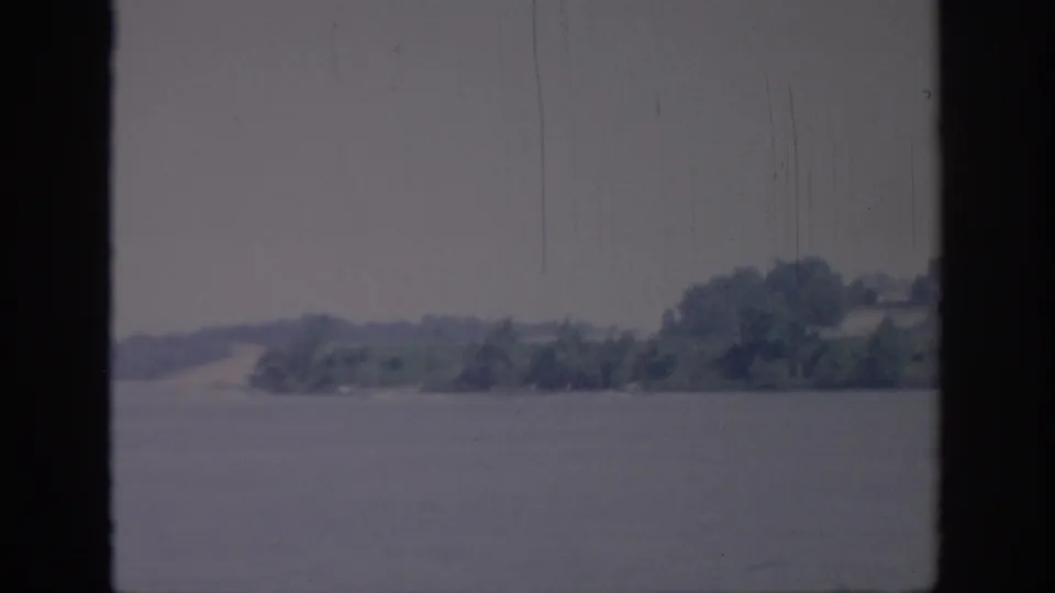 1967 Oklahoma 8mm frame showing a broad body of water and a distant wooded shoreline under muted sky.