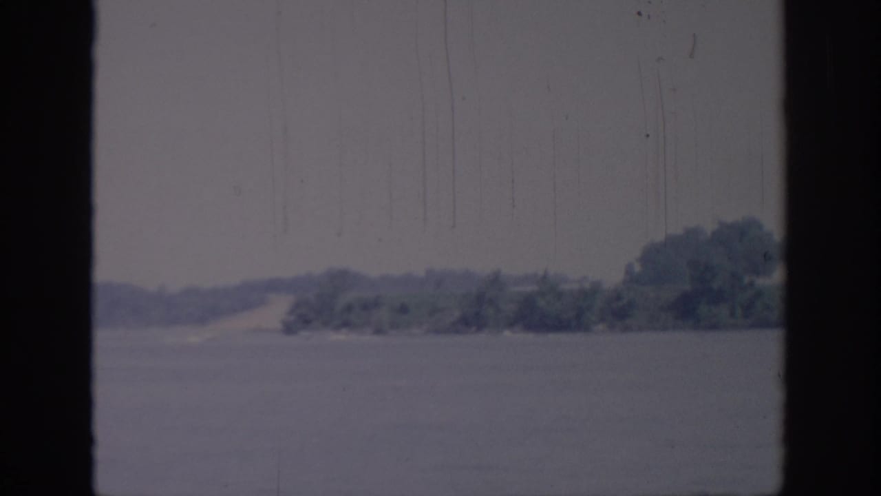 Distant wooded shore across calm water, bordered by dark film edges.