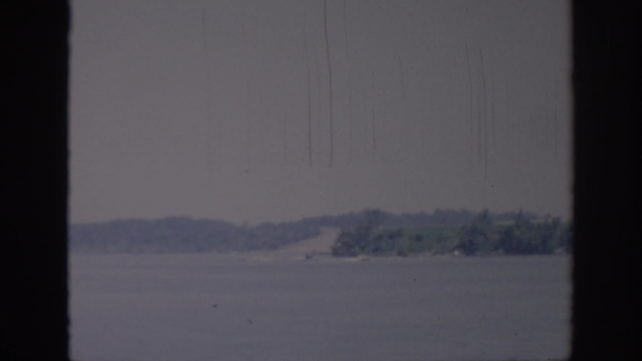 Final 1967 Oklahoma frame holding on water and a distant wooded shore, with aged 8mm texture visible.