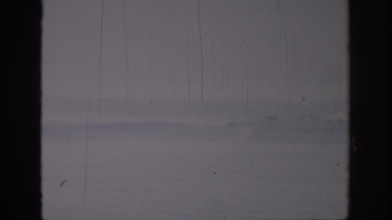 Soft 8mm frame from Oklahoma, 1967, with calm water, a far shoreline, and the view split by a dark window mullion.